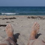 eileen's feet in the sand with the ocean in the background