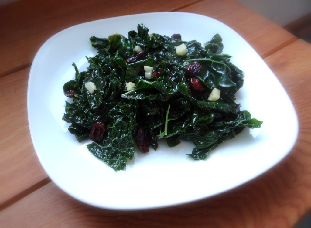 cooked kale with garlic and cranberries, served on a white plate