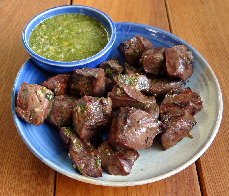 serving plate with the cooked beef heart and a dipping bowl of chimichurri sauce