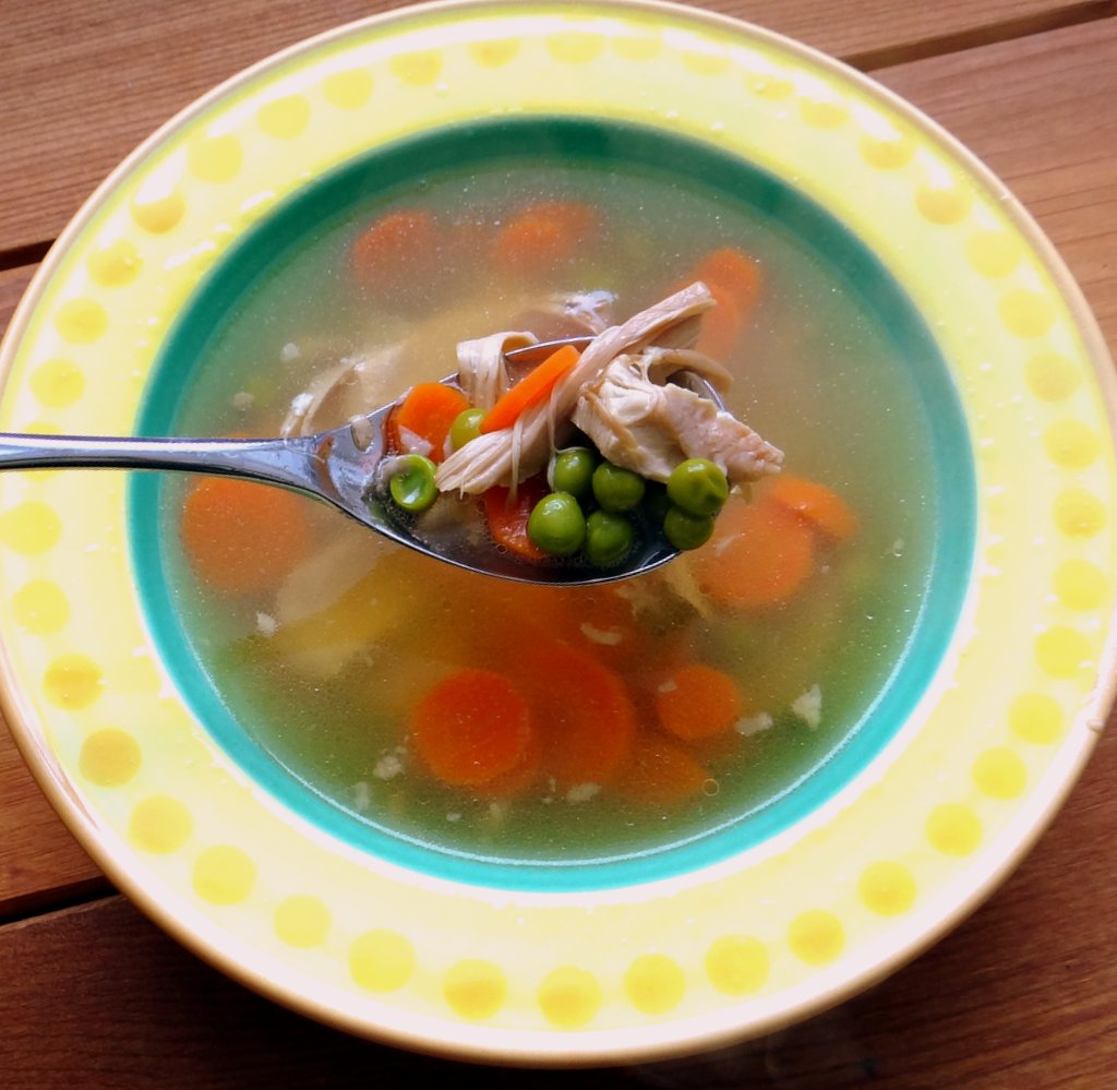 The soup served in a yellow and blue bowl, with a spoon full of chicken and vegetables