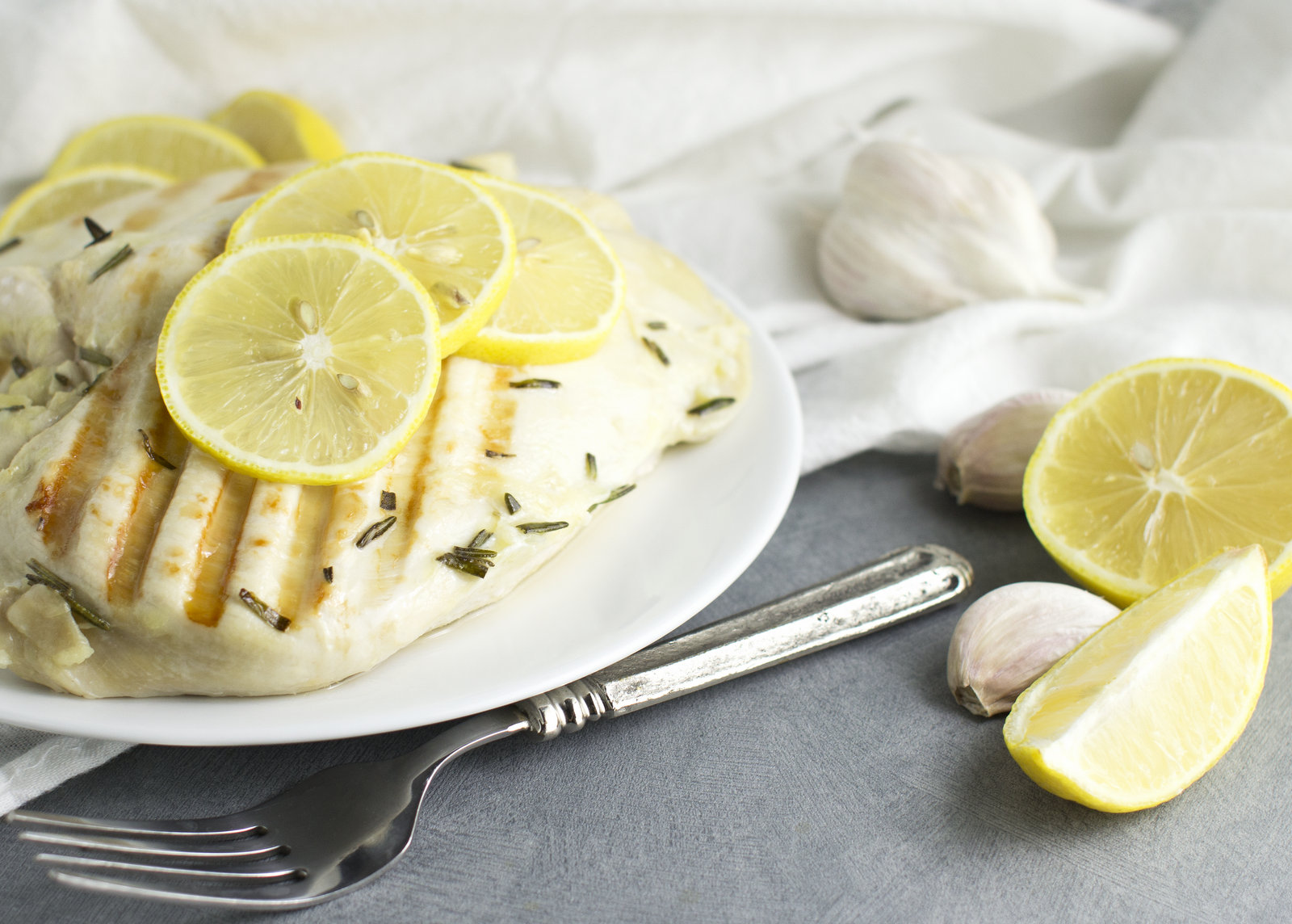 grilled chicken on a white plate with lemons on the side