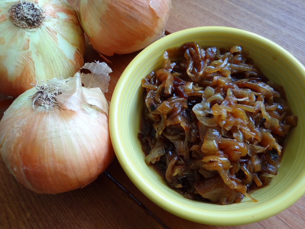 bowl or caramelized onions with some whole raw onions alongside in comparison