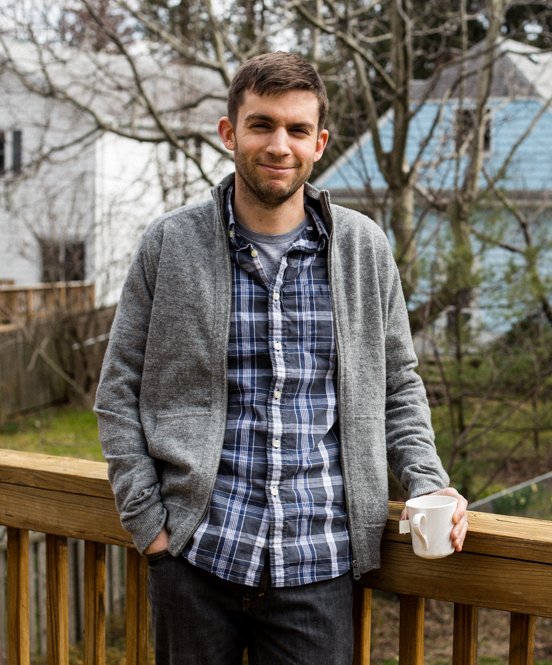 Russ on his back porch drinking a cup of tea and wearing a beard and a plaid shirt