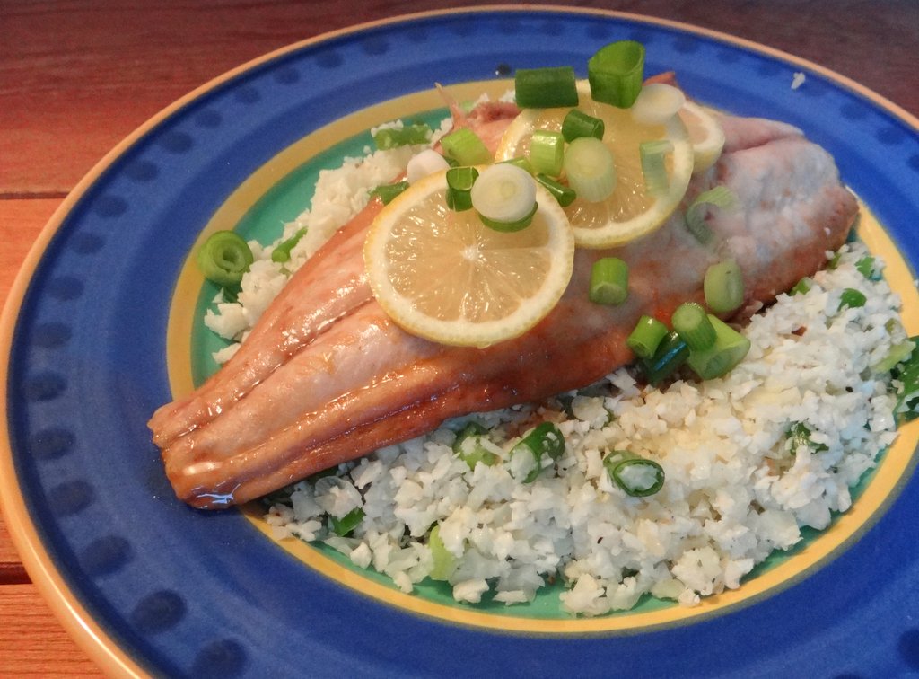 cooked mackerel served on top of cauliflower rice with scallions and sliced lemons on top