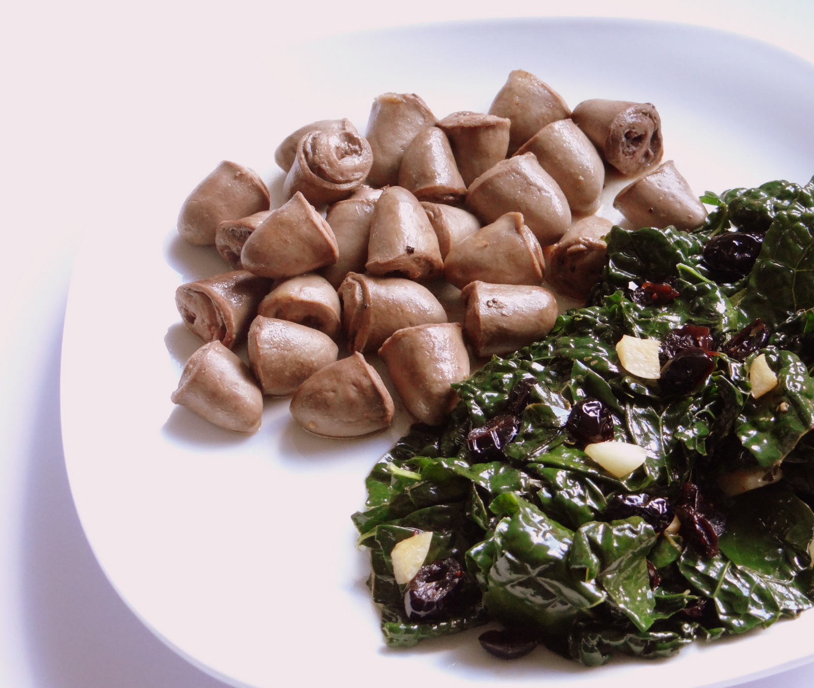 cooked chicken hearts on a plate alonside saueteed kale