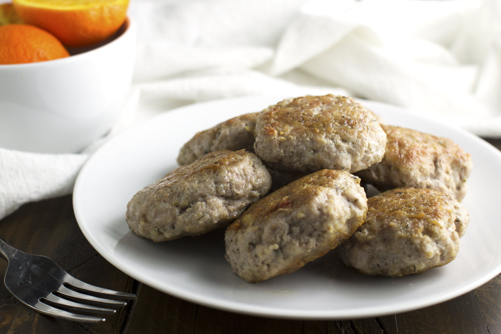 sausage patties on a white plate with sliced oranges in the background