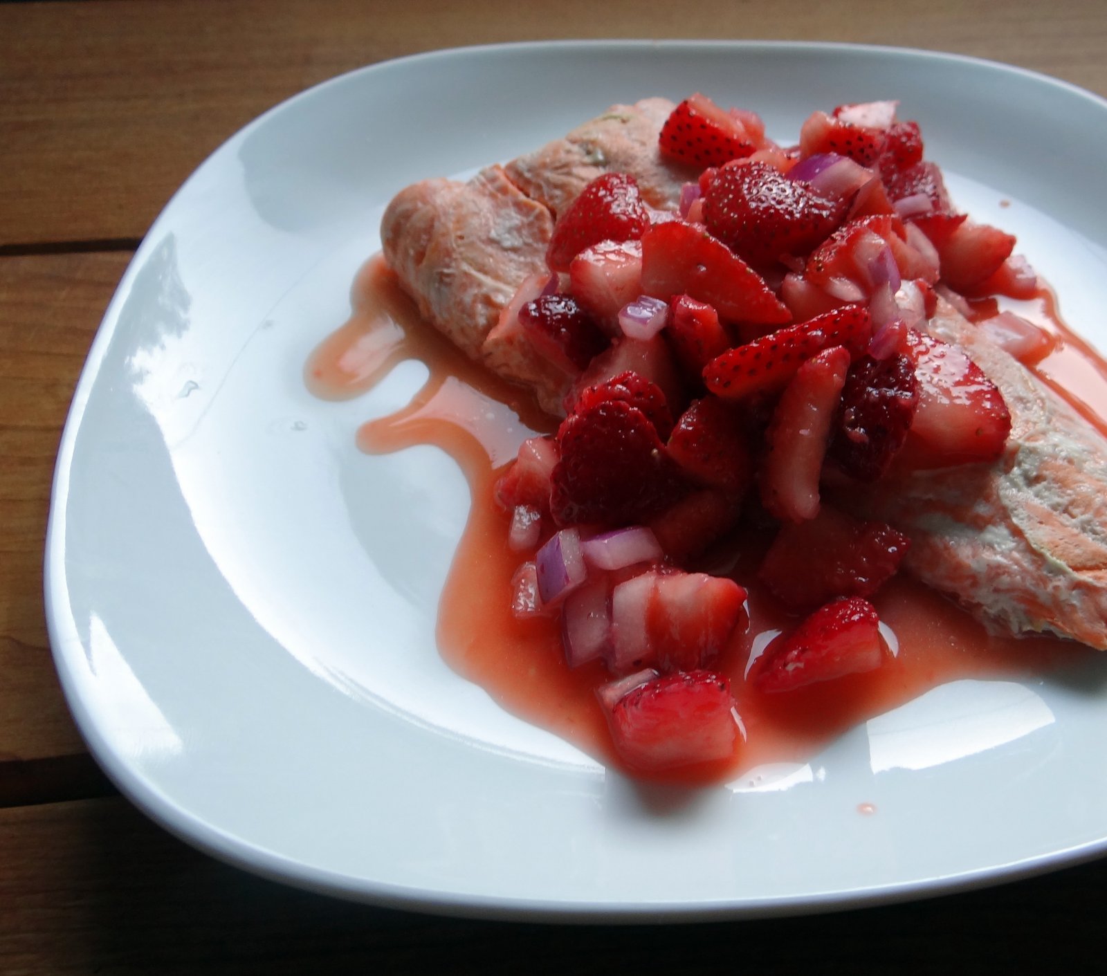 cooked salmon on a white plate, with strawberry salsa on top