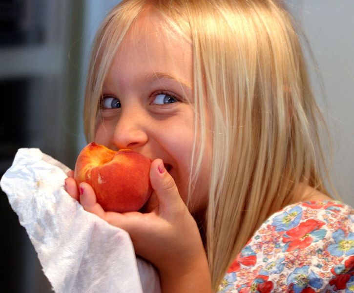 young girl smiling as she eats a peach