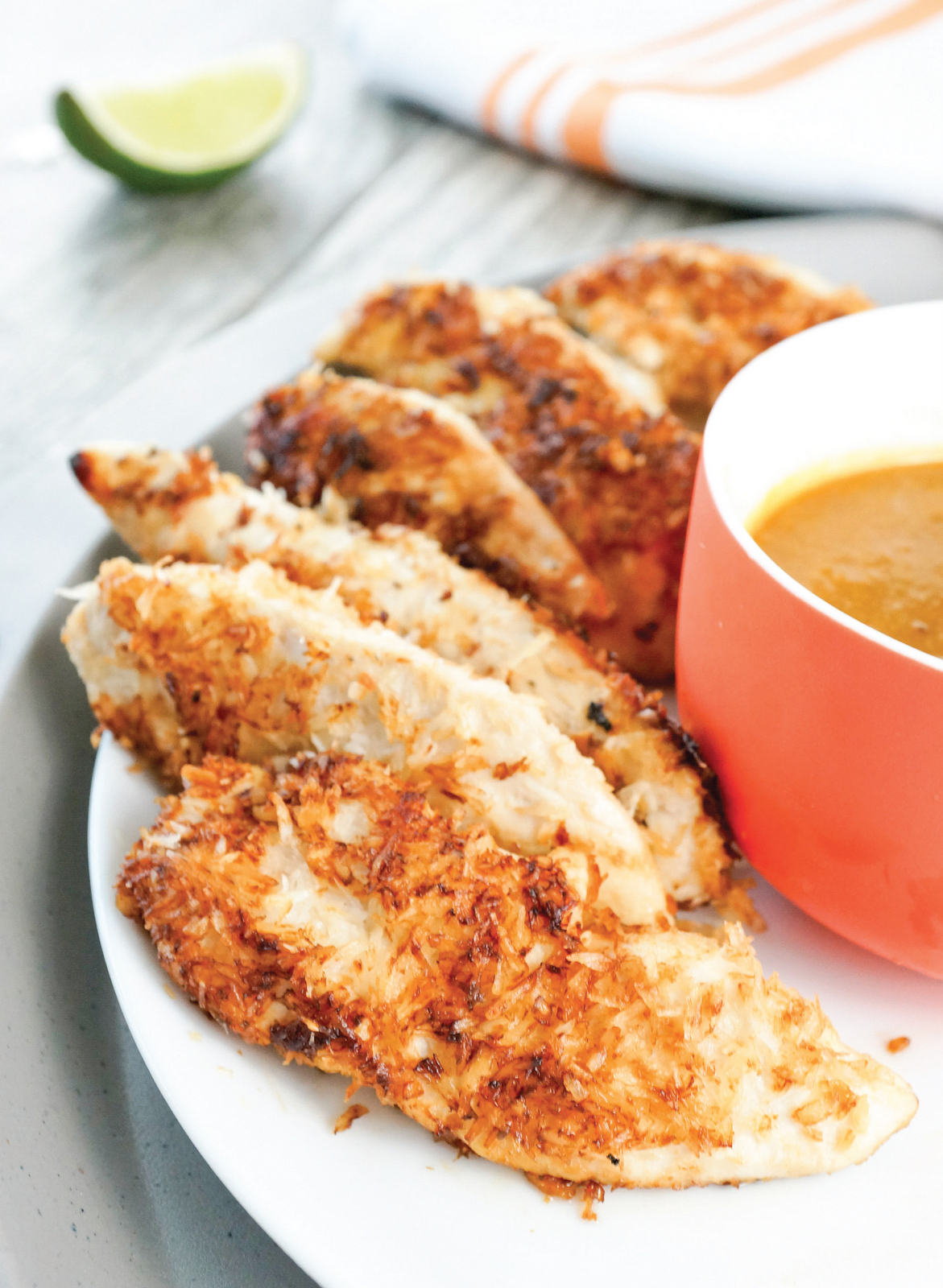 cooked chicken tenders on a white plate with a bowl of dipping sauce beside them