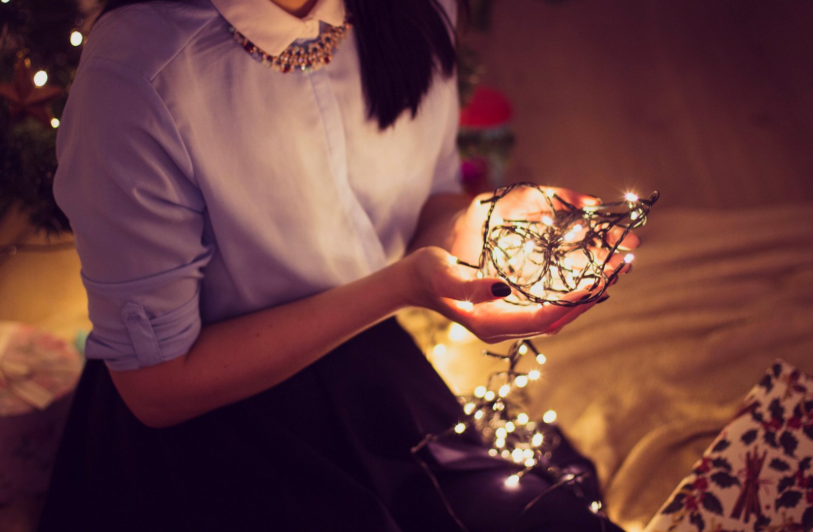 woman sitting, holding white holiday lights in her cupped hands