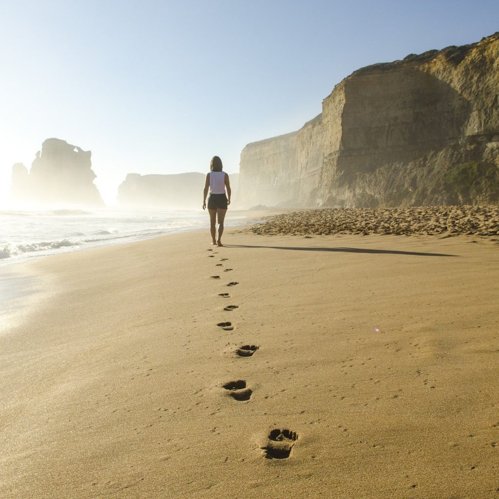 woman walking on a beach, footprints in the sand behind her