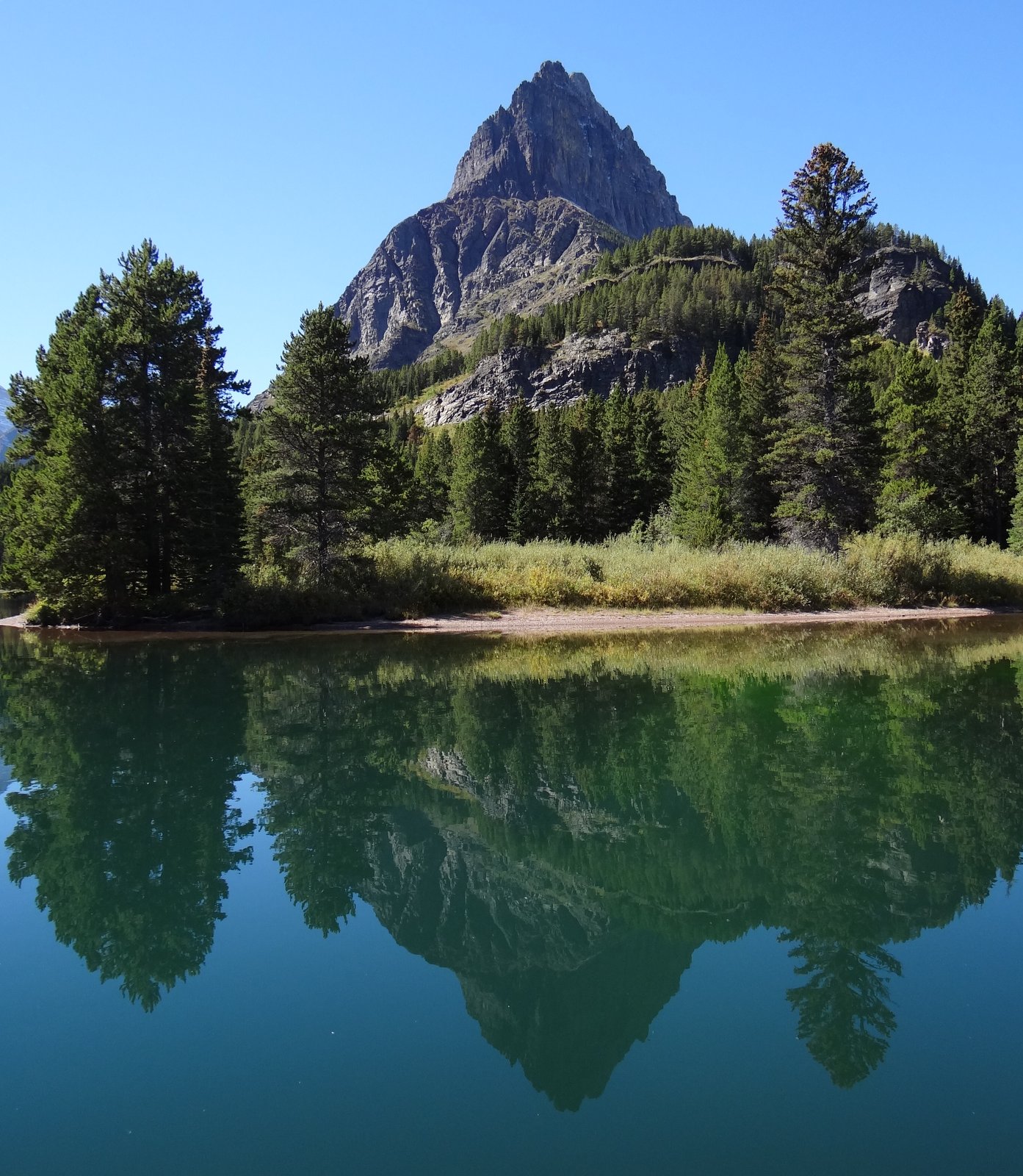 Mountain under a blue sky with a mirror image reflected in a lake