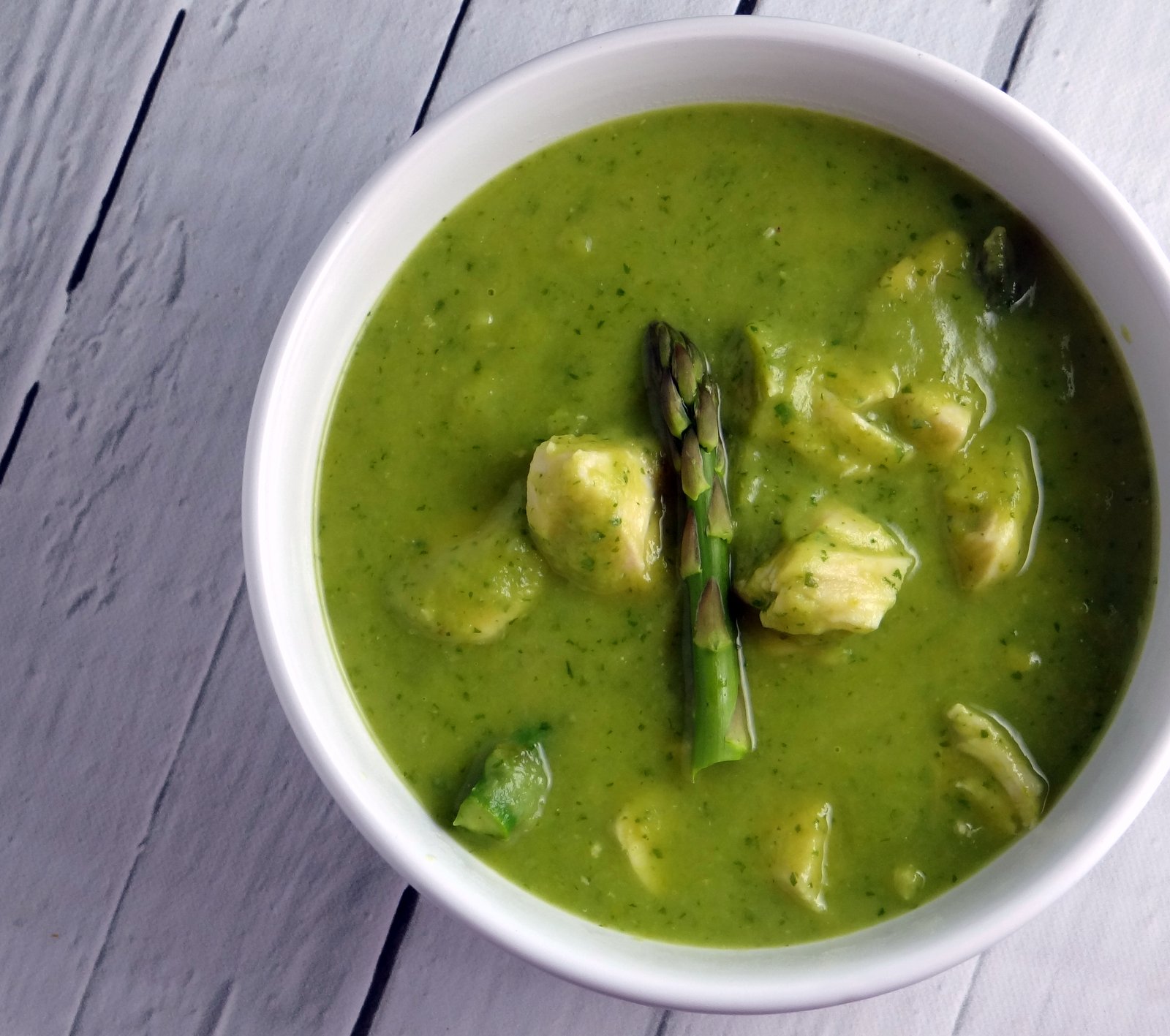 a bowl of creamy, richly green soup with big chunks of chicken and asparagus tips