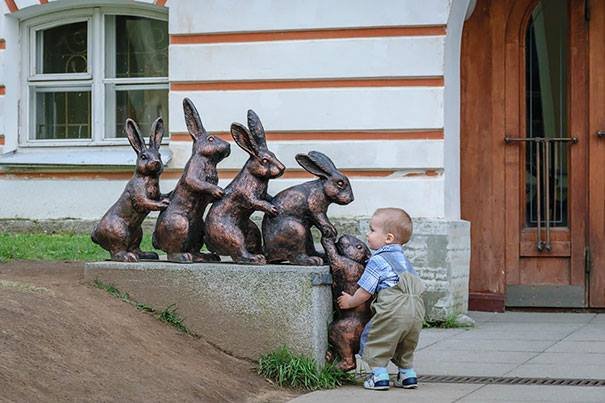 Sculpture of a rabbit family with baby rabbit needing a lift, and a little boy in real life trying to help