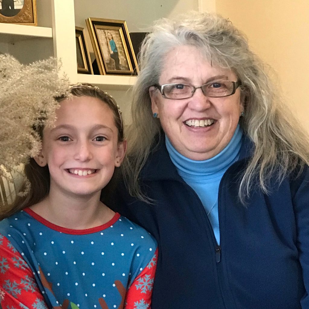 Donna smiling with long grey hair, standing next to her granddaughter