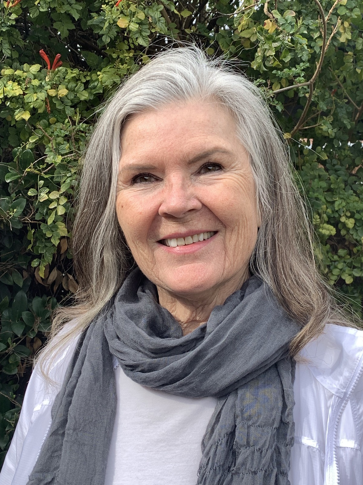 Headshot of Debra, with long grey hair, white shirt, and grey scarf