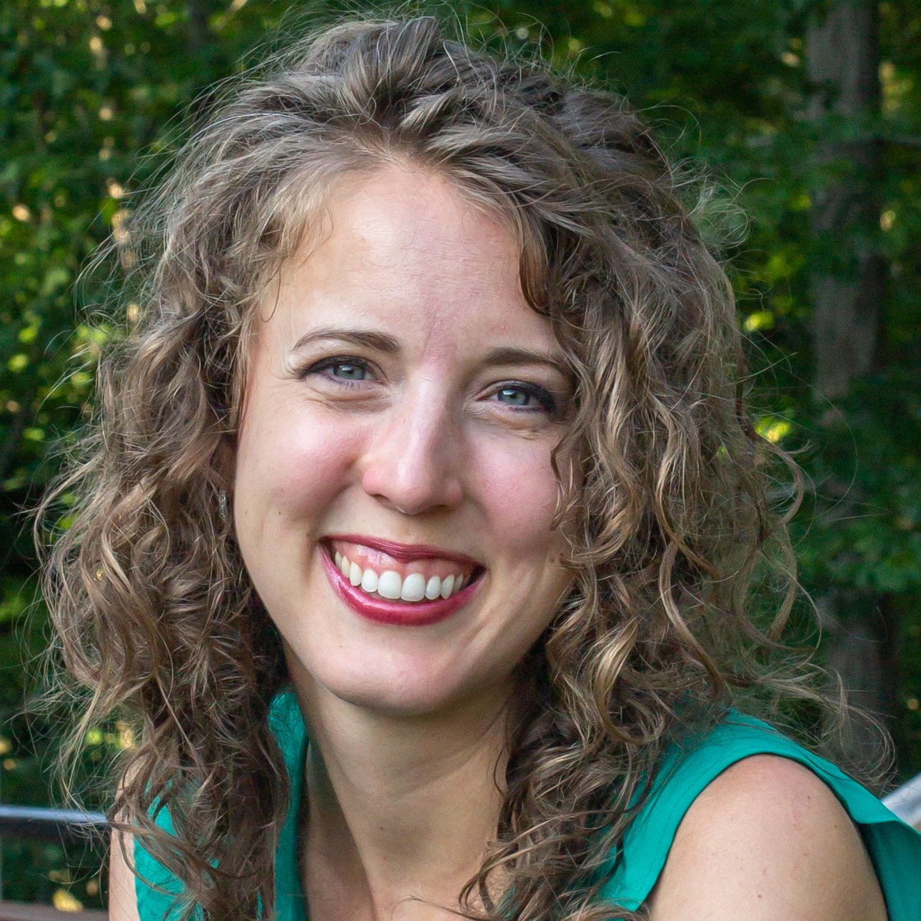 Headshot of Emily, smiling with long curly hair and wearing a teal sleeveless shirt