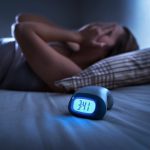 Woman lying in bed with hands over face, clock says 3:41am