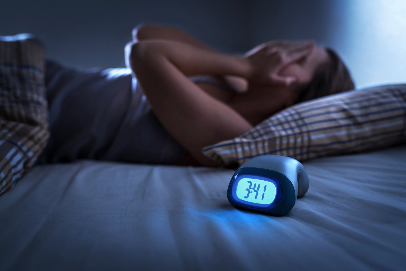 Woman lying in bed with hands over face, clock says 3:41am