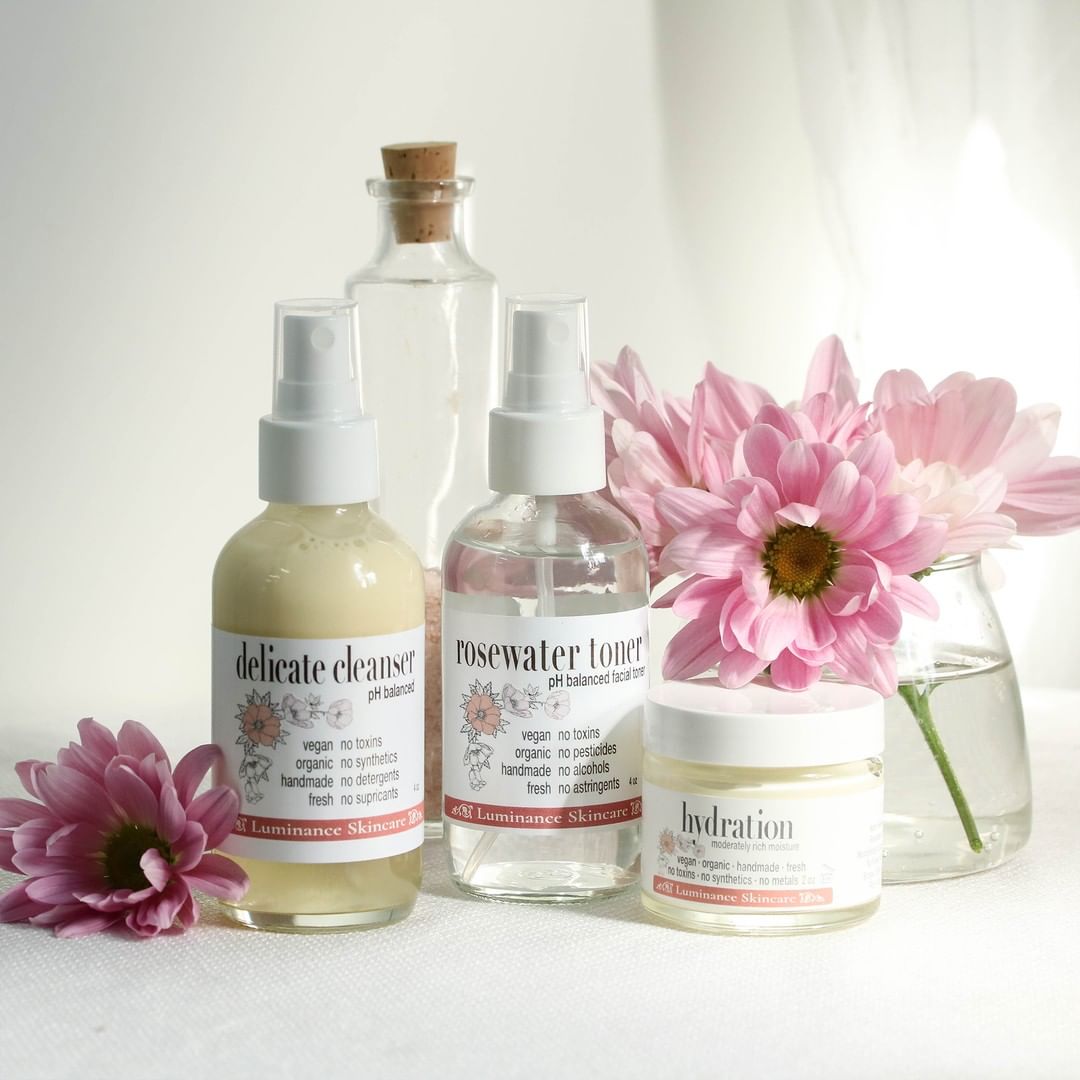 glass bottles of cleanser, toner, cream with pink flowers alongside