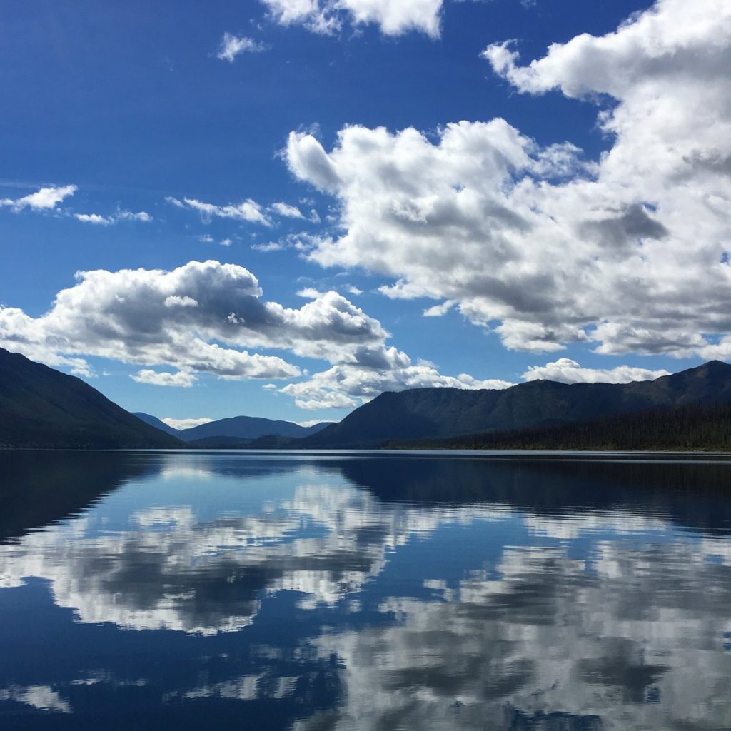 a bright blue sky with white clouds reflected on a lake