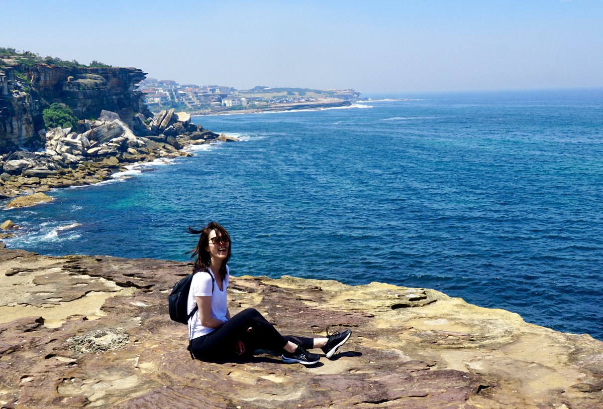 Evelyn sitting a cliff overlooking the ocean, laughing with the wind blowing through her hair