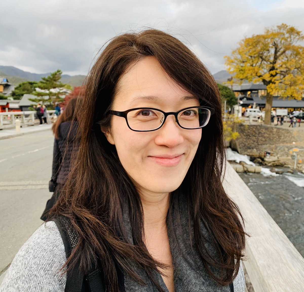 Headshot of Evelyn with long brown hair, wearing glasses and grey sweater