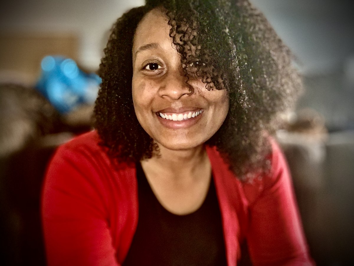 Tameka smiling, wearing a black t-shirt and red sweater