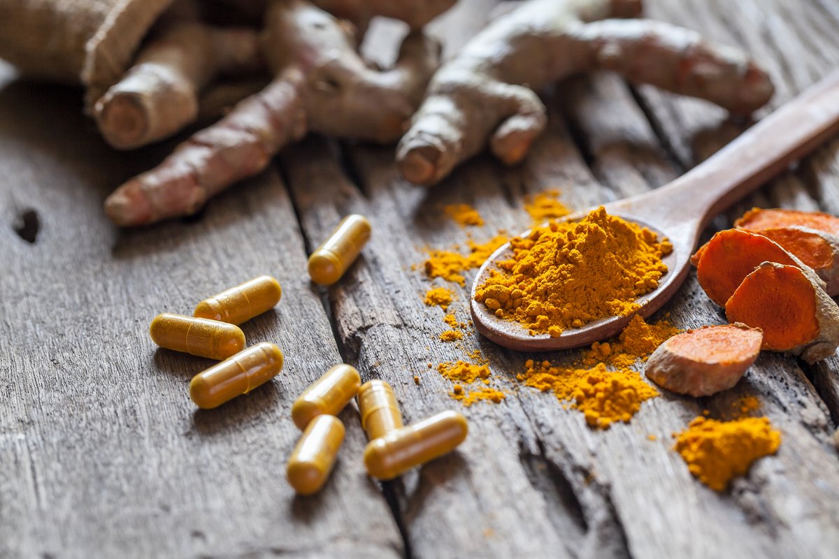 turmeric rhizomes, powder, and capsules on a wooden background