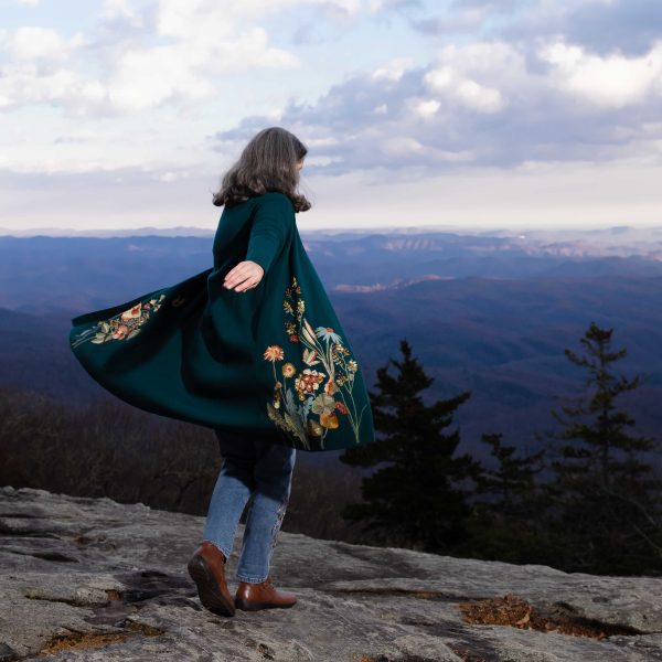 author dancing on a mountaintop, arms out, sweater coat swirling like a cape