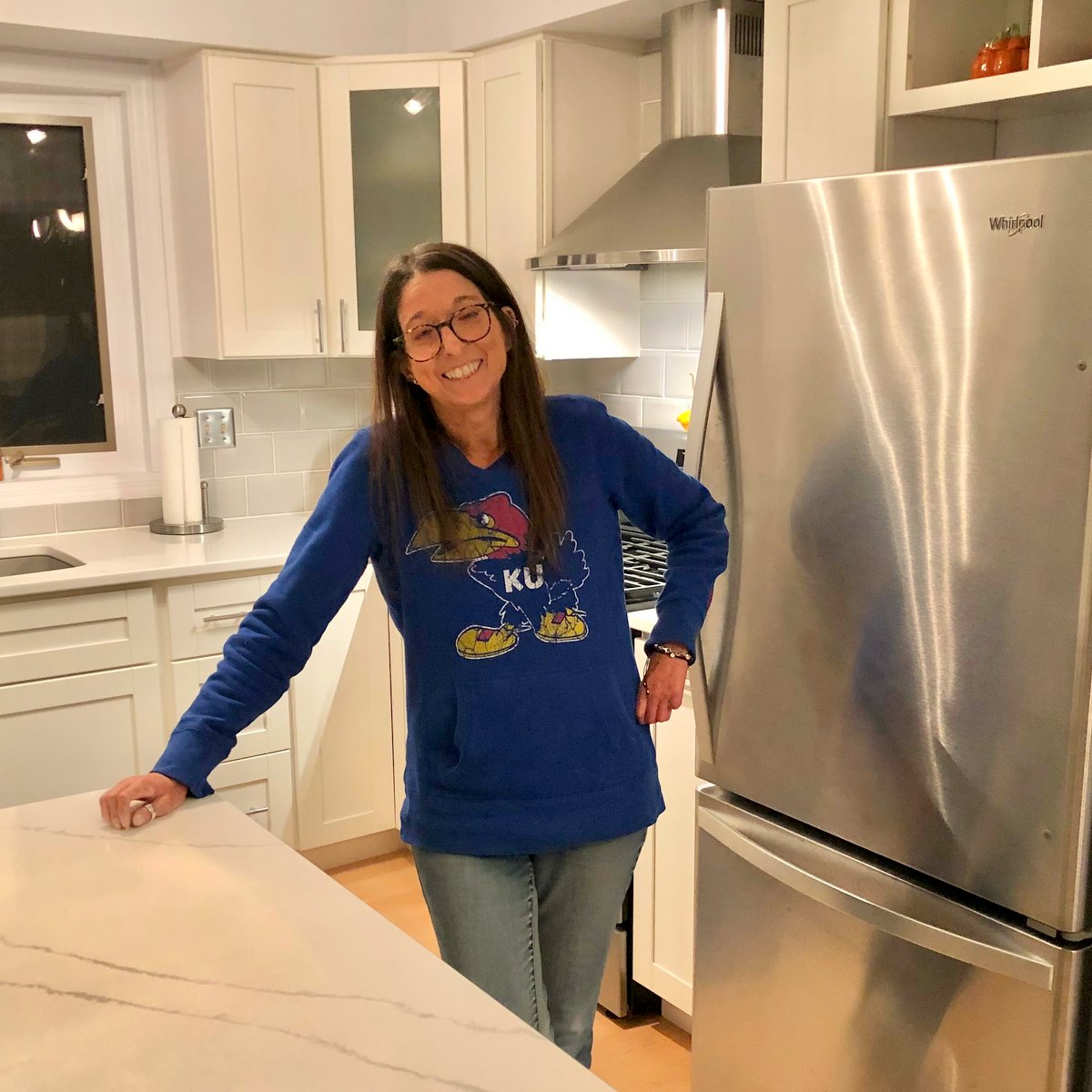 Ann smiling in her kitchen wearing a kansas jayhawks shirt - a favorite sports team