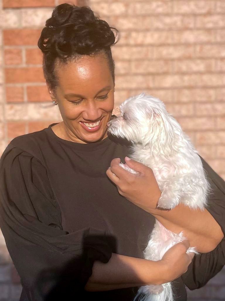 Marie smiling and gazing down at her small dog in her arms