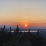 sunset over a low mountain range with lakes and trees in the foreground