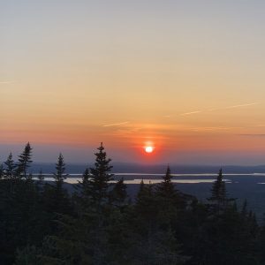 sunset over a low mountain range with lakes and trees in the foreground