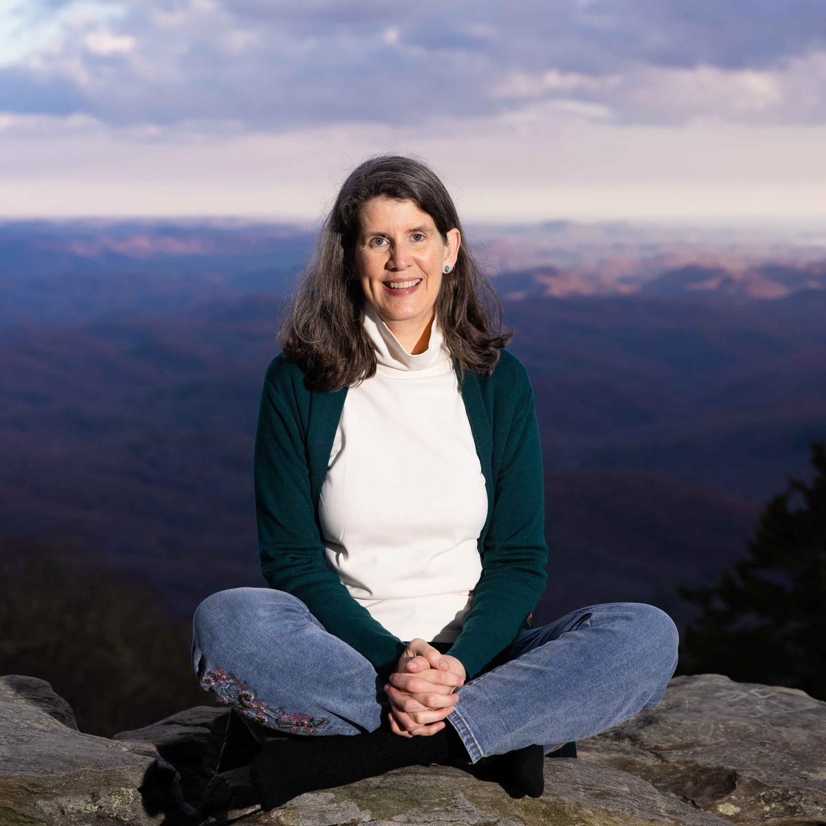 author sitting on a rock cross-legged with mountain vista behind her
