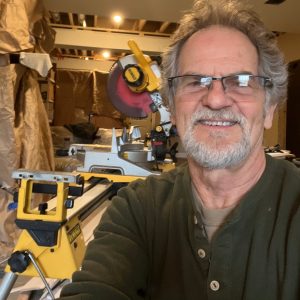 Neil in his workshop, smiling with grey hair and a beard