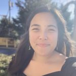 Emma smiling outside in filtered sunlight - long brown hair,