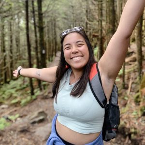 Emma hiking, arms raised and smiling big