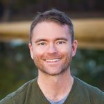 Robb outside, smiling, with a blurred nature background behind him